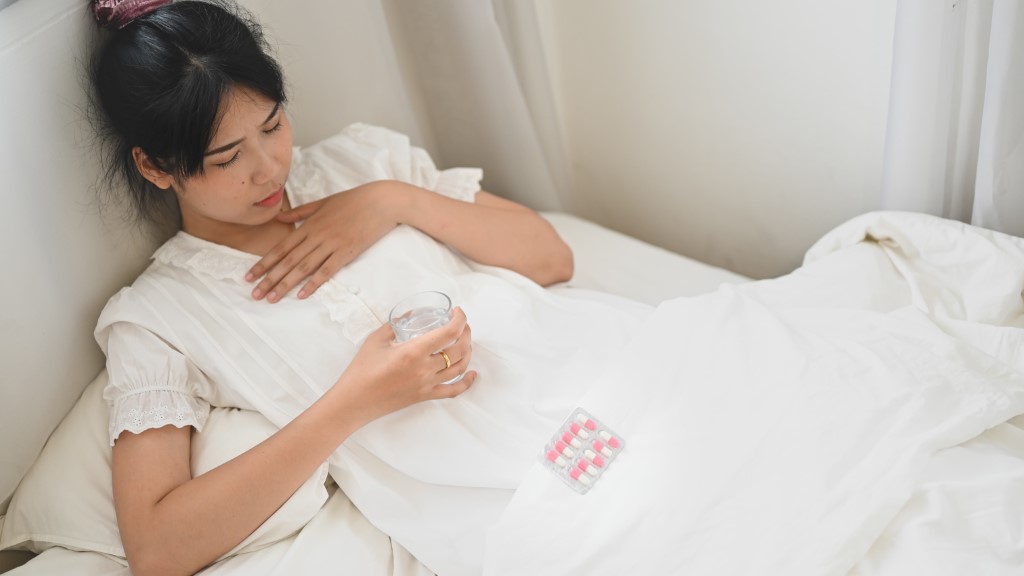 Kobieta w jasnej piżamie leży w zrelaksowanej pozycji na materacu w nowoczesnej sypialni. W tle widać łóżko, co sugeruje komfort i wypoczynek.